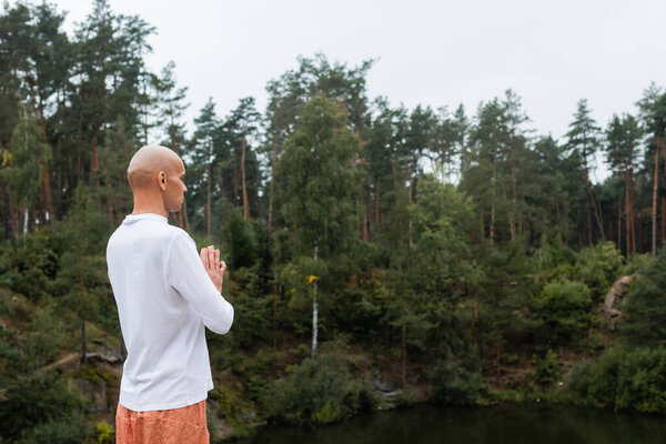 Буддист в белой толстовке молится над озером в лесу