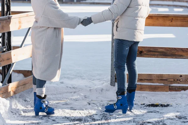 坐在冰鞋里的年轻夫妇手牵手靠近外面的冰场 — 图库照片