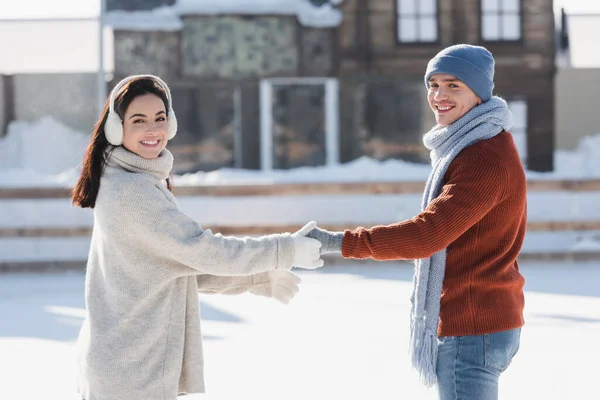 Leende Ung Kvinna Hörselkåpor Håller Hand Med Glad Pojkvän Ishallen — Stockfoto