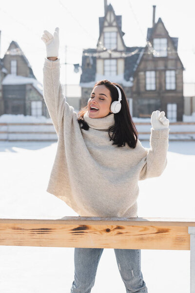 happy young woman in wireless headphone listening music and singing on ice rink 