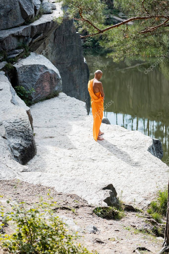 high angle view of buddhist monk meditating near rocks over forest lake