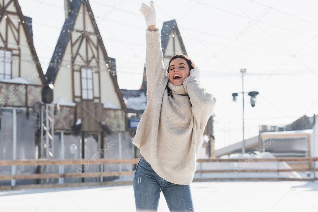 happy young woman in wireless headphone singing while listening music on ice rink 