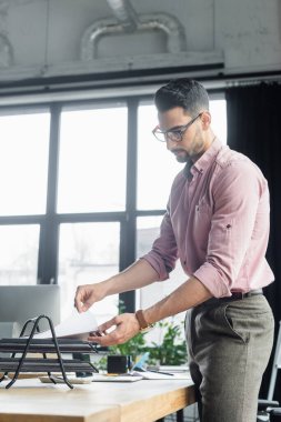 Genç Müslüman işadamı masadaki tepsiden kağıtları alıyor. 