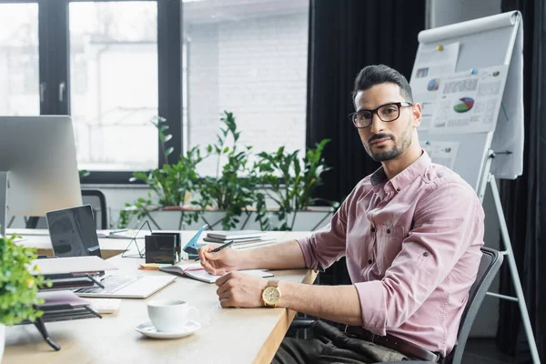 Moslim Zakenman Zoek Naar Camera Buurt Van Kopje Koffie Laptop — Stockfoto