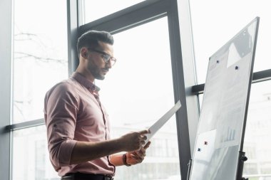 Gözlüklü Arap işadamı ofiste kağıt parçalarına bakıyor. 