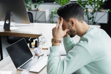 Müslüman iş adamının ofisteki buruşmuş kağıdın yanında boş ekranla dizüstü bilgisayara bakışının yan görüntüsü 