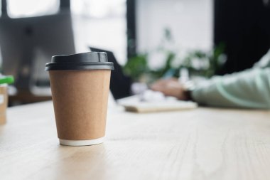 Ofisteki bulanık işadamının yanındaki kağıt bardağın kırpılmış görüntüsü 