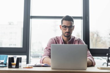 Gözlüklü Müslüman işadamı ofiste dizüstü bilgisayar ve hesap makinesi kullanıyor. 