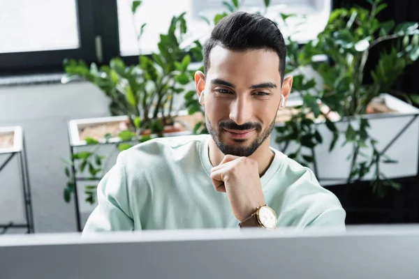 Lachende Arabische Zakenman Draadloze Oortelefoons Zoek Naar Wazig Computer Monitor — Stockfoto