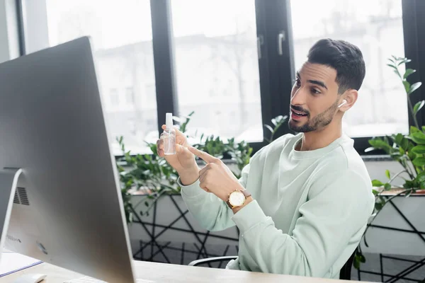 Hombre Negocios Musulmán Sonriente Auriculares Apuntando Mano Desinfectante Cerca Computadora — Foto de Stock