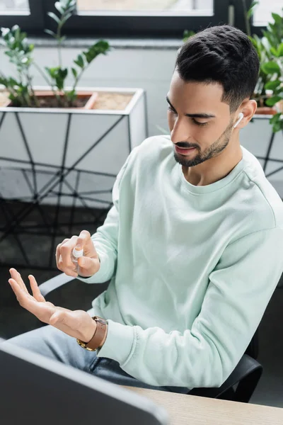 Giovane Uomo Affari Arabo Auricolare Utilizzando Disinfettante Mano Vicino Computer — Foto Stock