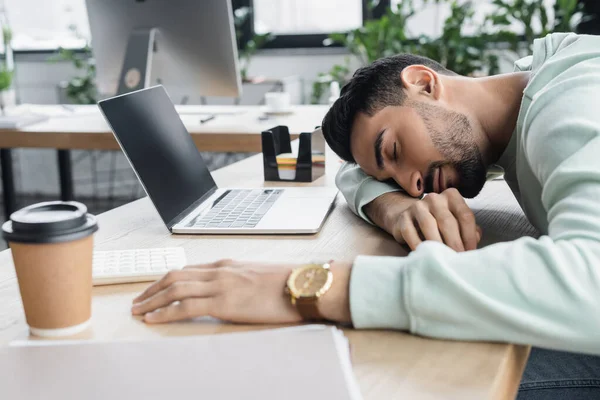 年轻的阿拉伯商人睡在咖啡旁 在办公室里用笔记本电脑 — 图库照片