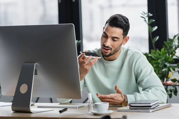 Hombre Negocios Musulmán Grabando Mensaje Audio Teléfono Inteligente Cerca Computadora —  Fotos de Stock