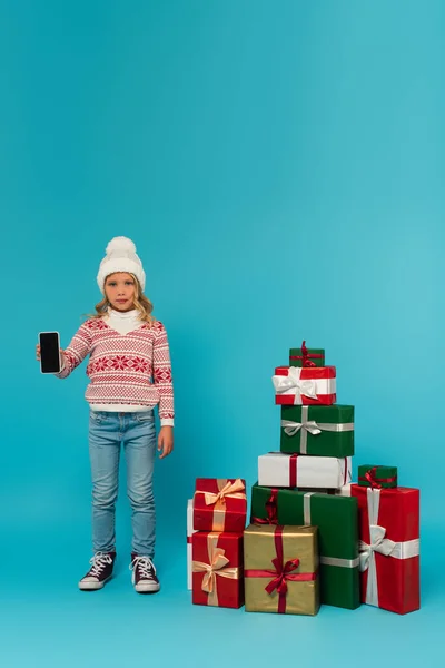 Ребенок Тёплом Свитере Джинсах Показывает Смартфон Чистым Экраном Рядом Подарками — стоковое фото