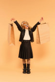 full length view of trendy girl with tiger face painting holding shopping bags on beige