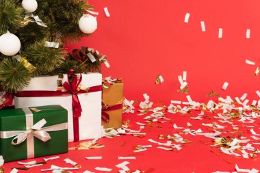 Noel ağacının altında kırmızı üzerine konfeti dökülürken sunulan hediyeler