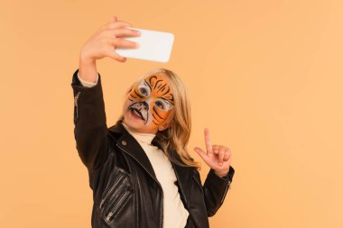 Kaplan yüzlü çocuk bejde izole edilmiş selfie çekerken parmağıyla işaret ediyor.