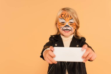 Kaplan makyajlı gülümseyen kız bej renkli bulanık akıllı telefondan selfie çekiyor.