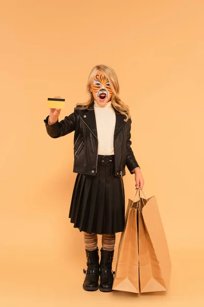 脸上涂满老虎的孩子 购物袋和信用卡在米黄色上咆哮 — 图库照片