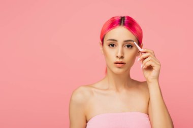 Genç bir kadın, boyalı saçlarıyla cımbız tutarken pembe kaşlarını şekillendiriyor. 