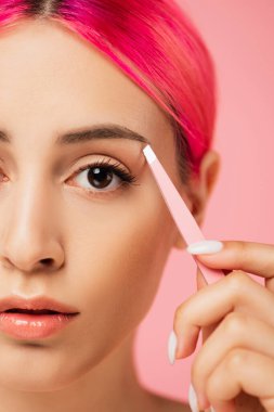 Pembe kaş şekillendirirken cımbızla boyanmış saçları olan genç bir kadın. 