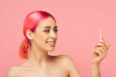Pembe üzerine izole edilmiş cımbızlara bakan renkli saçlı neşeli genç bir kadın. 