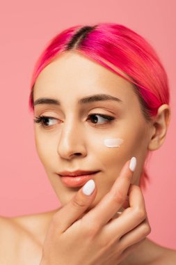 Pembeye izole edilmiş yüz kremi süren boyalı saçlı genç bir kadın. 