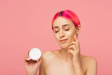 Saçları boyalı, elinde kabı olan ve pembe bir yüz kremi süren mutlu genç bir kadın. 