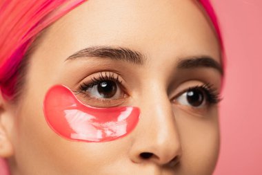 Pembe üzerinde boyalı saçlı ve kolajen göz bandı olan genç bir kadının kısmi görüntüsü 