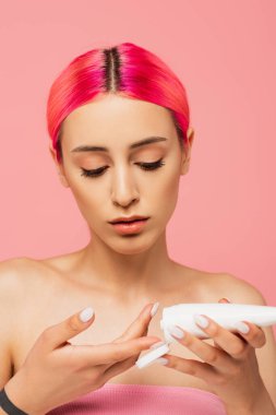 Pembeye izole edilmiş kozmetik ürünler uygularken elinde renkli saç tüpü olan genç bir kadın. 