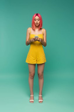 Turkuazda akıllı telefon kullanan pembe boyalı saçlı bir kadın.