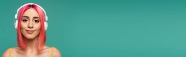 Pembe boyalı saçlı mutlu genç bir kadın kulaklıkla müzik dinliyor mavi, afişte izole edilmiş.