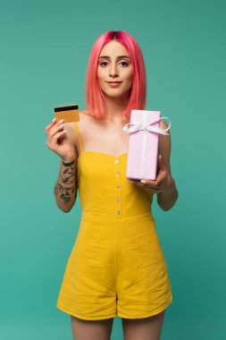Gülümseyen genç kadın pembe boyalı saçlarıyla hediyesini tutuyor ve kredi kartı mavi üzerine izole edilmiş. 