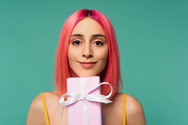 Pembe boyalı saçlarıyla gülümseyen genç kadın mavi renge sarılmış hediyesini tutuyor. 