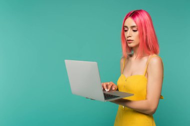 Pembe boyalı saçlı genç bir kadın mavi dizüstü bilgisayar kullanıyor. 