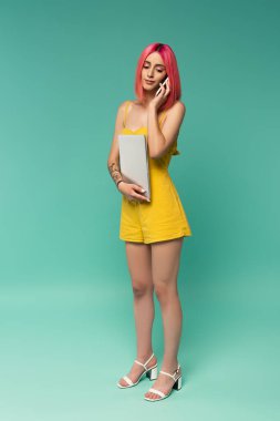 Pembe boyalı saçlı, dizüstü bilgisayarı olan ve mavi telefonda konuşan genç bir kadın. 