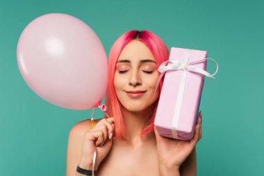 Pembe boyalı saçları olan mutlu genç bir kadın hediye paketi ve mavi üzerine izole edilmiş bir balon. 