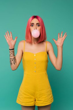 Şok olmuş, pembe boyalı saçlı genç bir kadın mavi sakız üflüyor. 