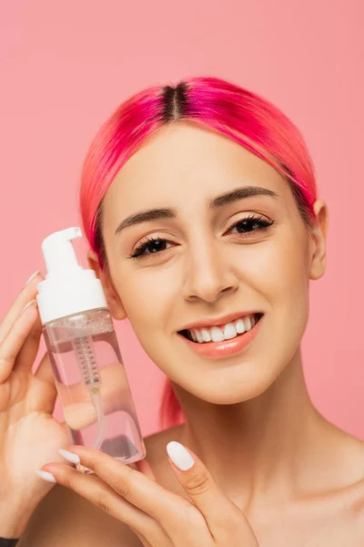ピンクに単離されたクレンジング製品とボトルを保持しながら カラフルな髪の笑顔を持つ若い女性の入れ墨 — ストック写真