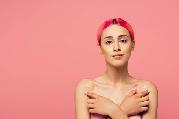 young woman with colorful hair applying lotion on bare shoulders isolated on pink 