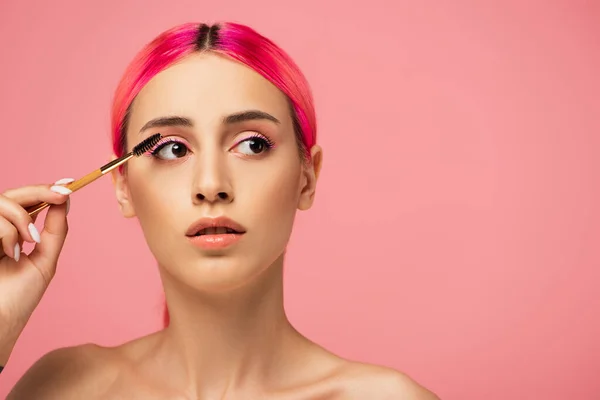 young woman with colorful hair styling eyebrow isolated on pink