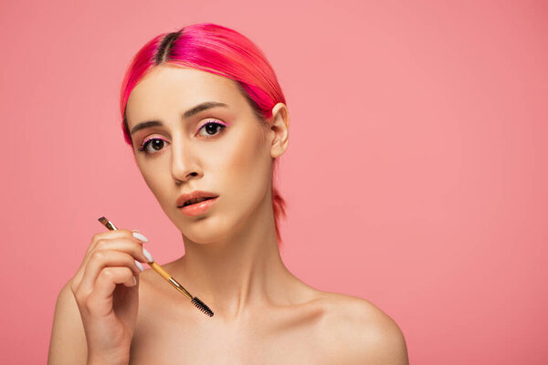 young woman with colorful hair holding eyebrow brush isolated on pink 