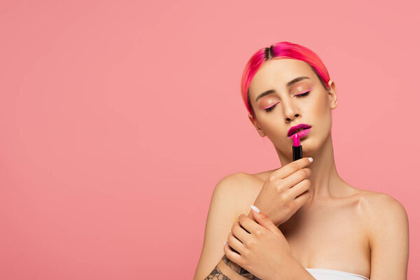 young woman with dyed hair and closed eyes applying lipstick isolated on pink 