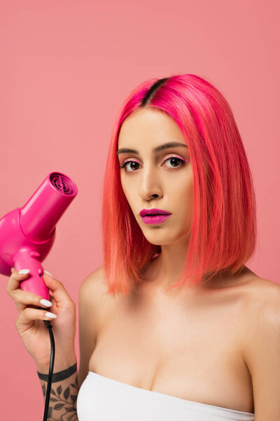 young woman with colorful hair holding hair dryer isolated on pink 