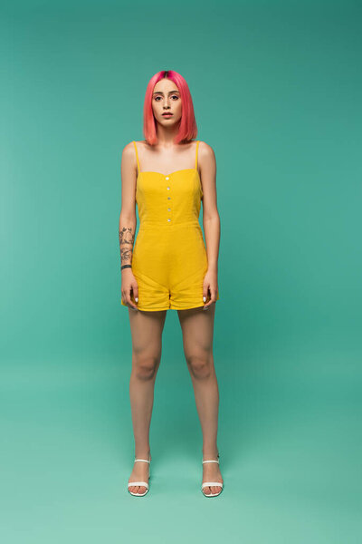 full length of young woman with pink dyed hair posing on turquoise
