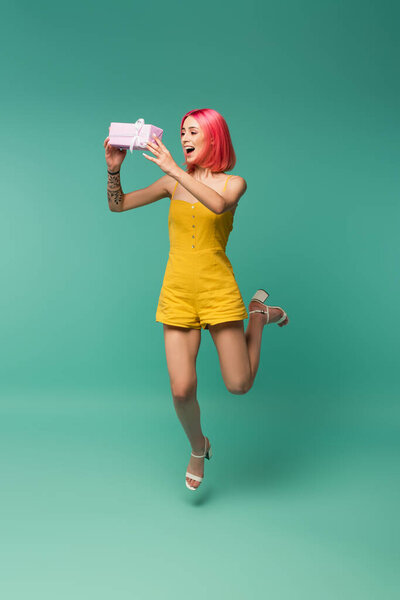 полная длина веселой молодой женщины с розовыми окрашенными волосами прыгать и ловить подарок на синий 