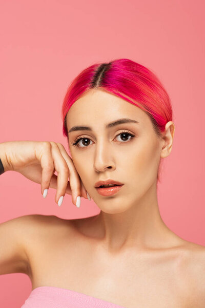 pretty young woman with colorful hair and bare shoulders looking at camera isolated on pink 