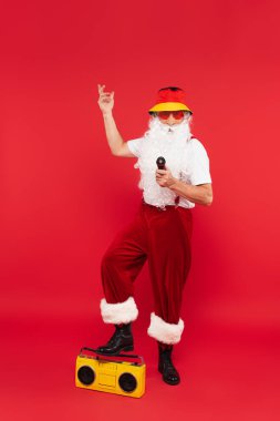 Kırmızı arka planda mikrofonlu, güneş gözlüklü Noel Baba.
