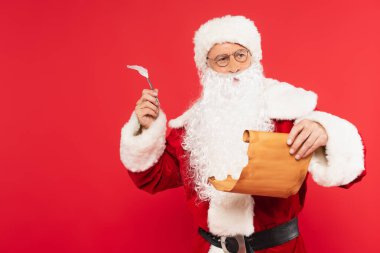 Kırmızı üzerinde duran kağıt ve kalemle düşünceli Noel Baba. 