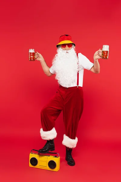 戴着太阳镜的圣诞爪 戴着帕纳马帽 在红色背景的啤酒盒旁拿着啤酒 — 图库照片
